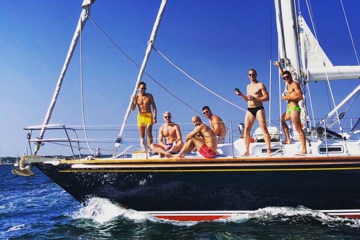 Group of mem standing and sitting on deck of sailboat