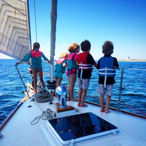 Group of kids standing at bow of sailboat looking out to ocean