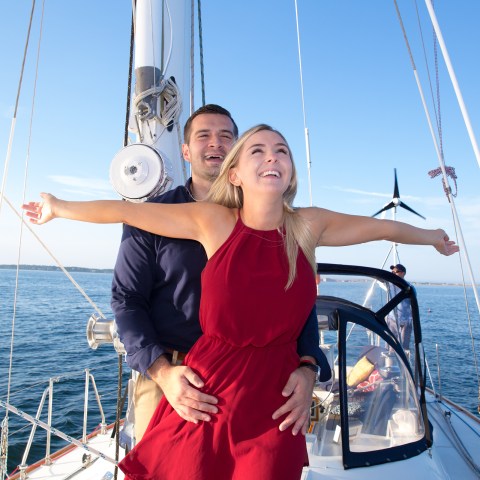 Man holding woman by the waist with her arms spread out on sailboat